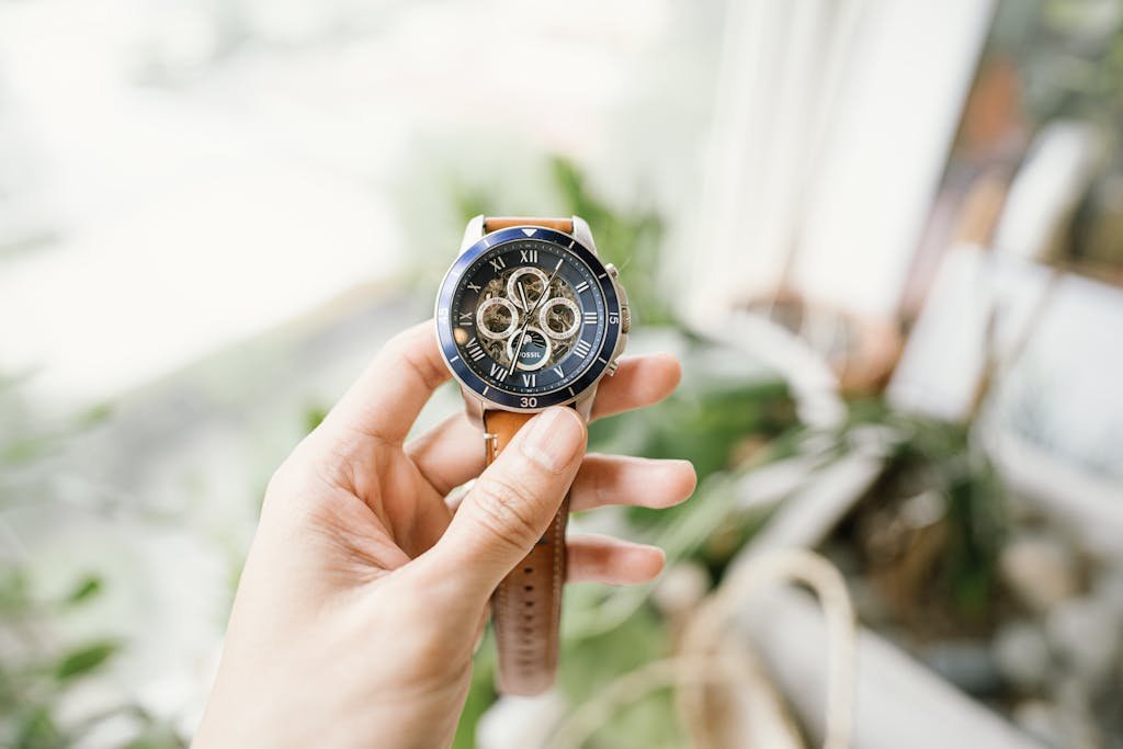 A hand holding a sophisticated wristwatch with intricate gears, featuring a blurred background.