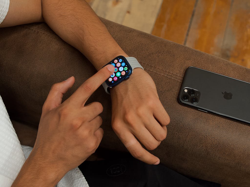 Close-up of a man using a smartwatch while a smartphone lies next to him on a sofa.